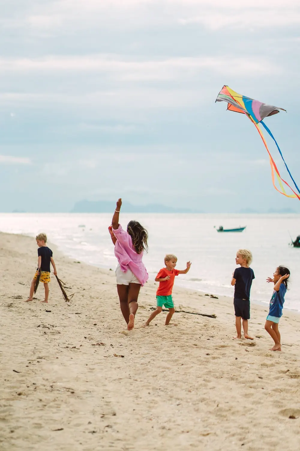 Children running along the sand together, flying a brightly coloured kite.